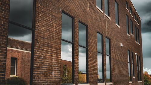Free Dramatic view of a brick building with reflective windows showing a stormy sky. Stock Photo