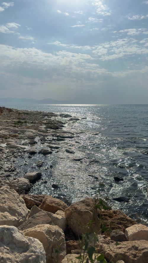 Free A serene view of a rocky coastline with sunlit sea under a partly cloudy sky. Stock Photo
