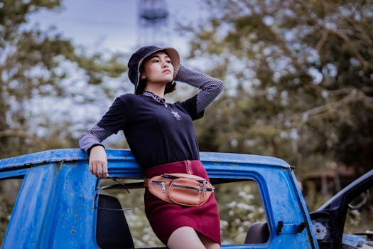 Stylish young woman stands confidently on an old blue car in nature.