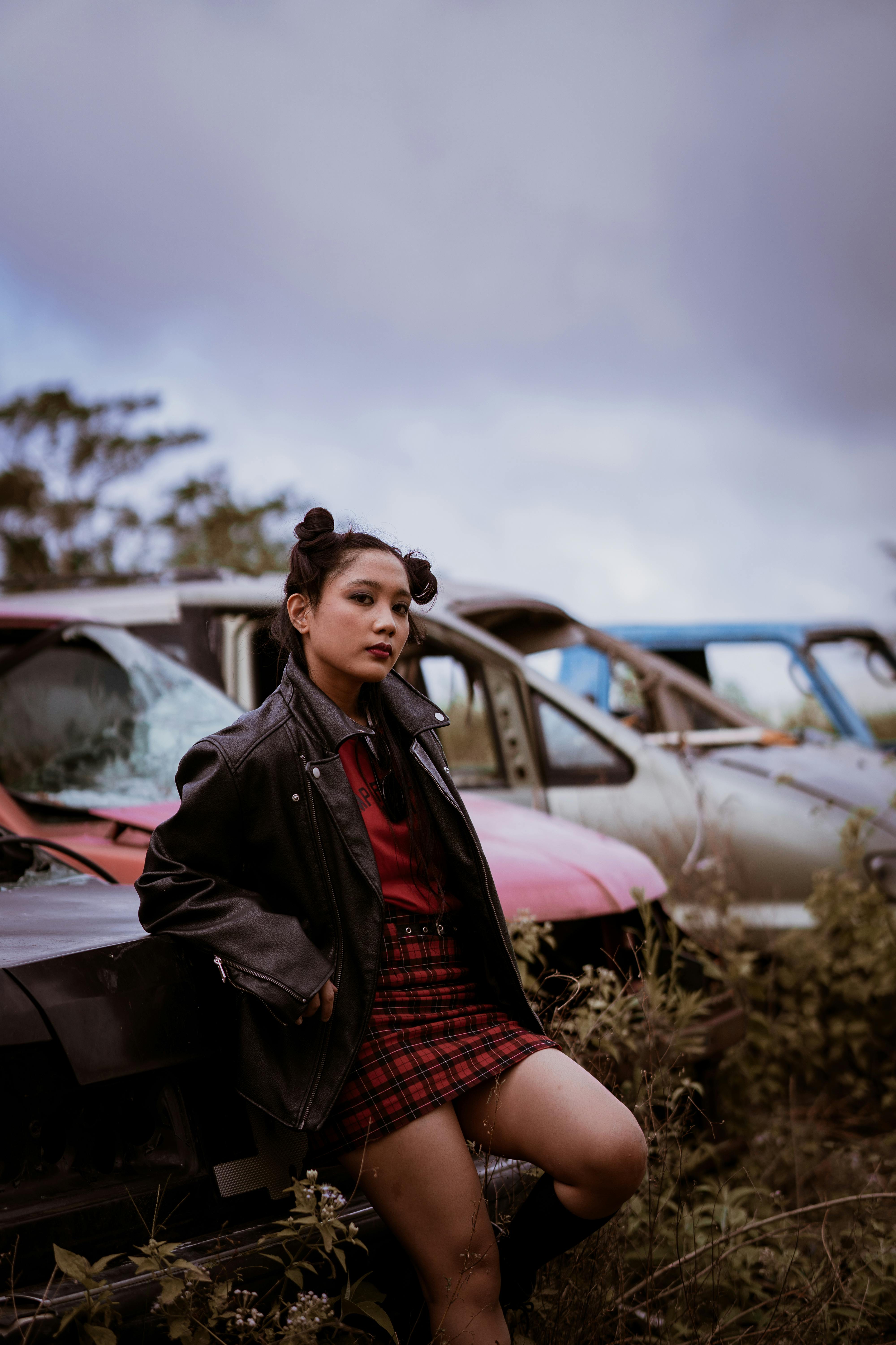 一位穿着皮夹克的时尚女子在废品站的古董车里摆姿势