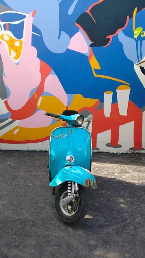 Free A classic turquoise Vespa scooter parked in front of a vibrant street art mural. Stock Photo
