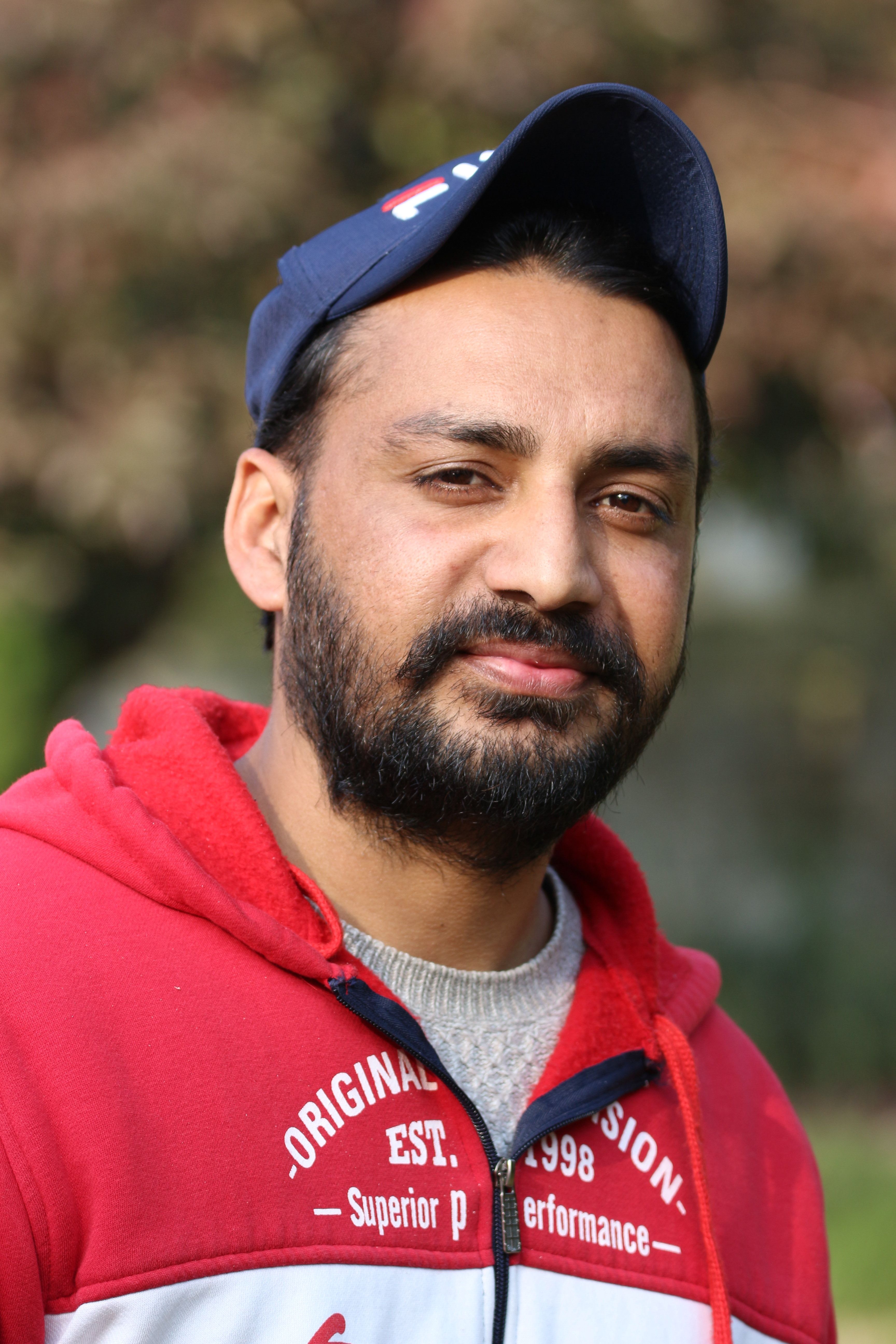 A man wearing a red hoodie and cap, posing in a casual outdoor setting.