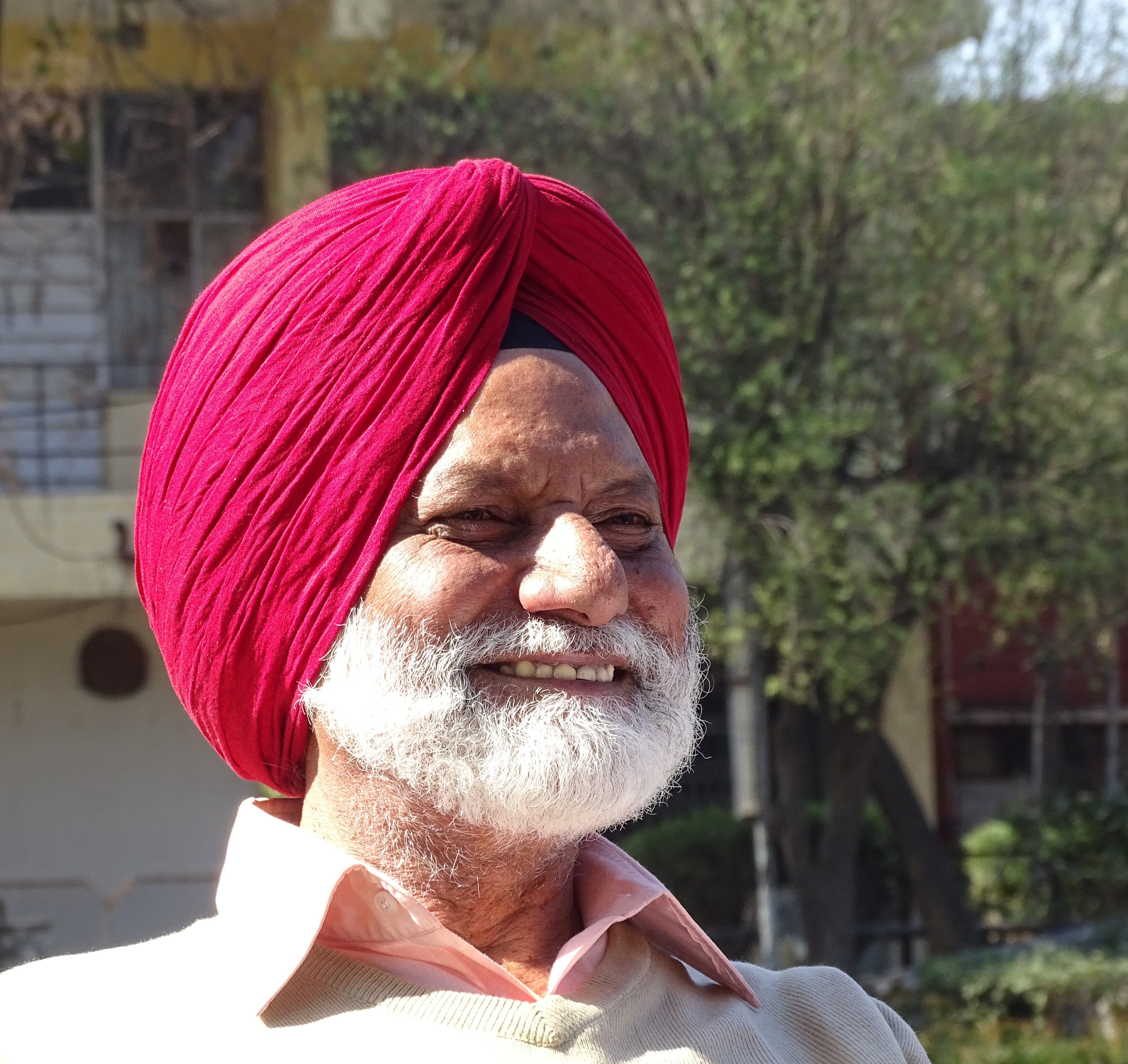 Senior South Asian man in a red turban smiling in outdoor setting, daytime.