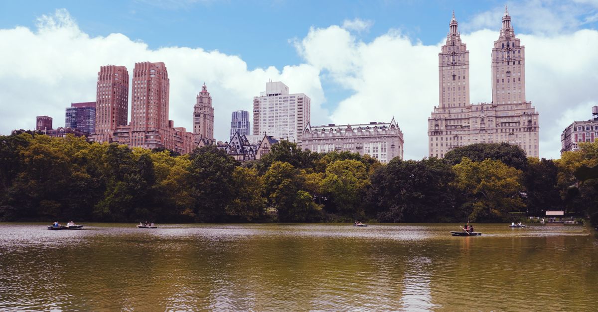 Breathtaking view of Central Park Lake with iconic Manhattan skyscrapers under a bright sky.