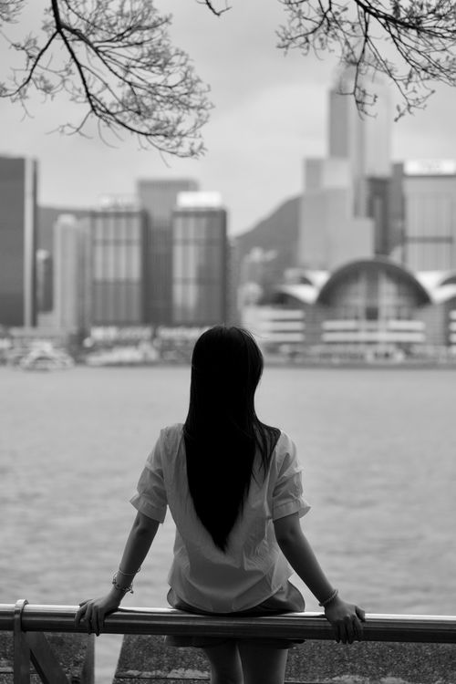 Free Woman gazes at the Hong Kong skyline from Victoria Harbor, black and white photo. Stock Photo