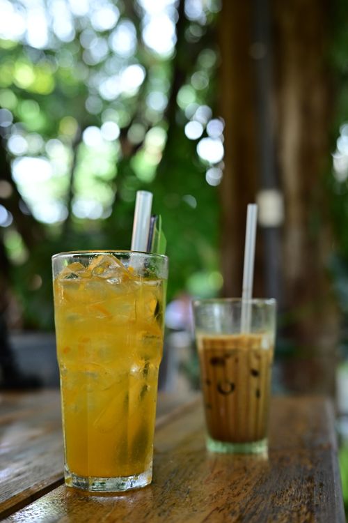 Free Close-up of iced tea and coffee on a wooden table with a lush outdoor background. Stock Photo