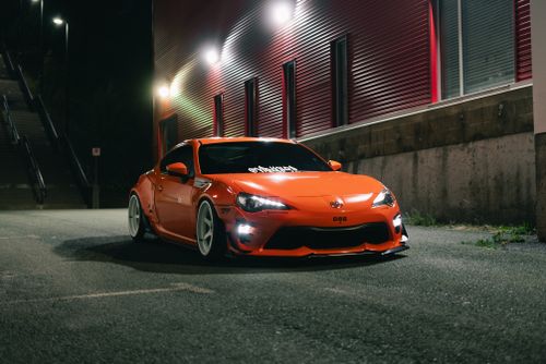 Free A sleek orange sports car parked in an urban setting at night, showcasing modern automotive design. Stock Photo