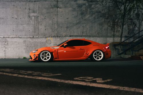 Free A vibrant orange sports car parked by a concrete wall under low light, highlighting its sleek design. Stock Photo