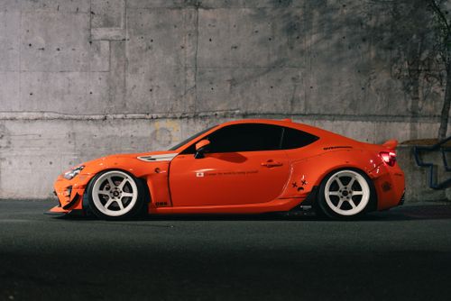 Free Stylish orange sports car parked against a concrete wall in a cityscape. Stock Photo