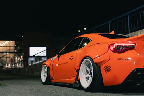 Free Sleek modified orange sports car parked on city street at night. Stock Photo