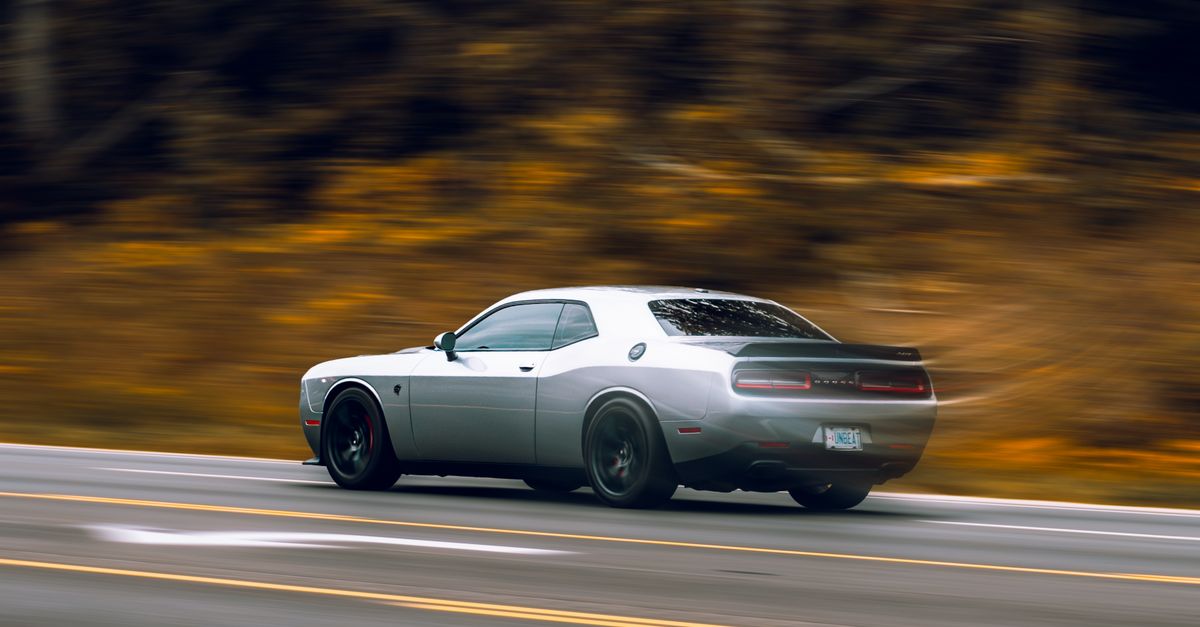 Dynamic shot of a gray sports car speeding on a highway with blurred autumn background.