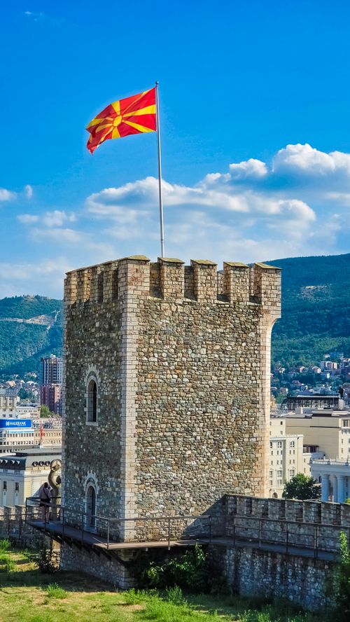 Free Stone fortress tower crowned with a Macedonian flag under bright blue skies in Skopje. Stock Photo