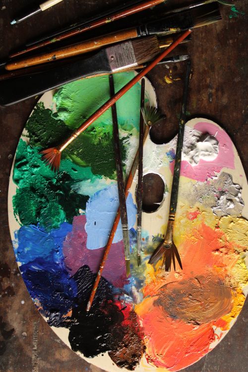 Free Vibrant artist palette with paint brushes displaying a spectrum of colors. Stock Photo