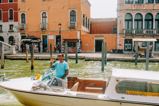 A man steers a water taxi through a scenic canal in Venice, Italy, on a sunny day.