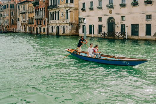 Three people on a traditional rowboat navigating a canal in Venice, Italy.
