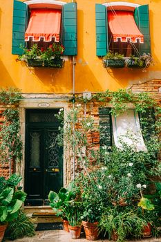 Charming facade of a colorful house in Italy with lush plants and vibrant window shades.