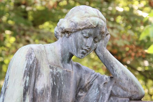 Free A serene sculpture of a woman deep in thought, surrounded by greenery. Stock Photo