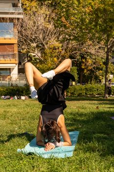 A person practices a headstand on a yoga mat in a sunny park setting, showcasing fitness and balance.
