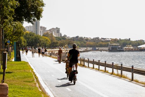 Free People biking and walking along a picturesque riverside path with cityscape in background. Stock Photo