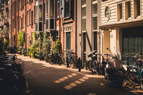 Free Picturesque Amsterdam street with bikes and sunlight, showcasing the city's unique architecture. Stock Photo