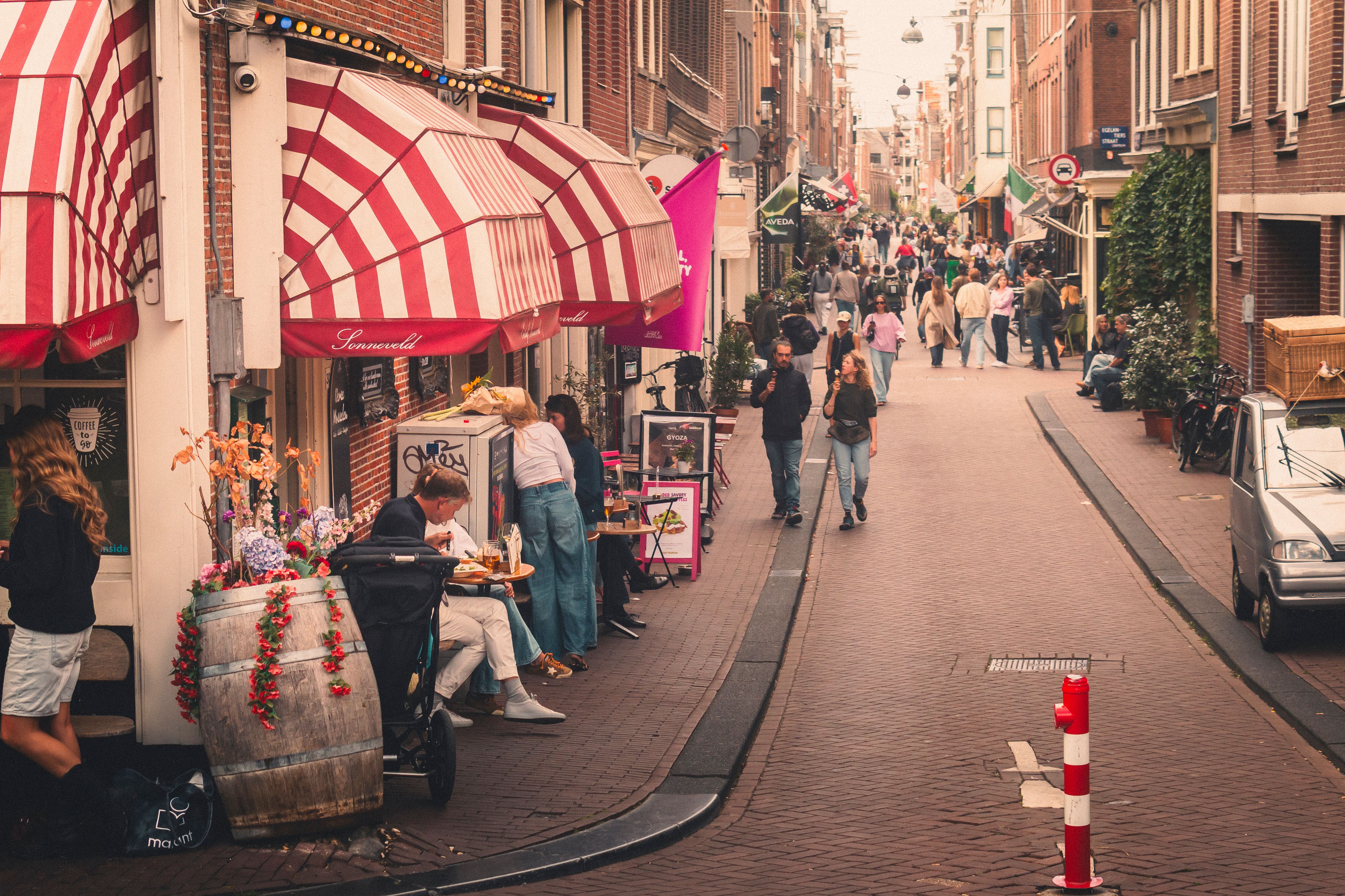 Lively street in Amsterdam bustling with people and vibrant shops, creating a cozy European atmosphere. - Fotografer Sidoarjo