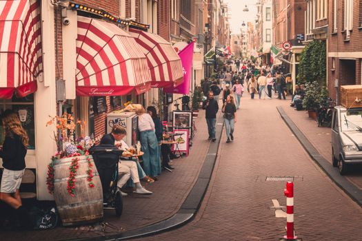 Rue animée d'Amsterdam, grouillante de monde et bordée de boutiques colorées, créant une atmosphère européenne chaleureuse.