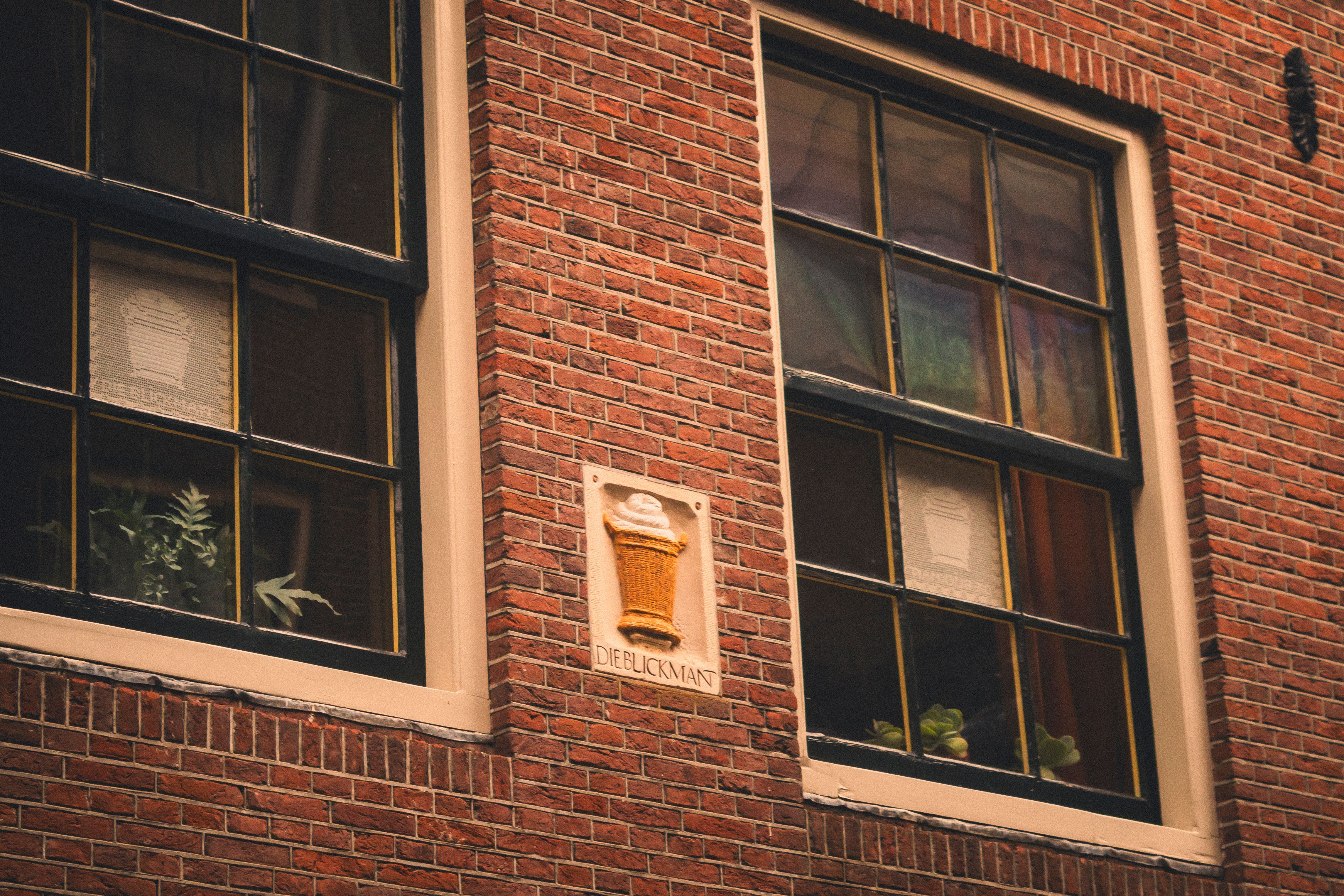 Close-up of a brick building facade in Amsterdam featuring a unique decorative element beside large windows.