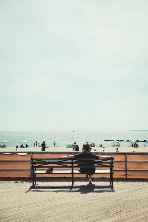 Free A tranquil scene of a person relaxing on a bench at Coney Island beach, capturing the essence of summer. Stock Photo