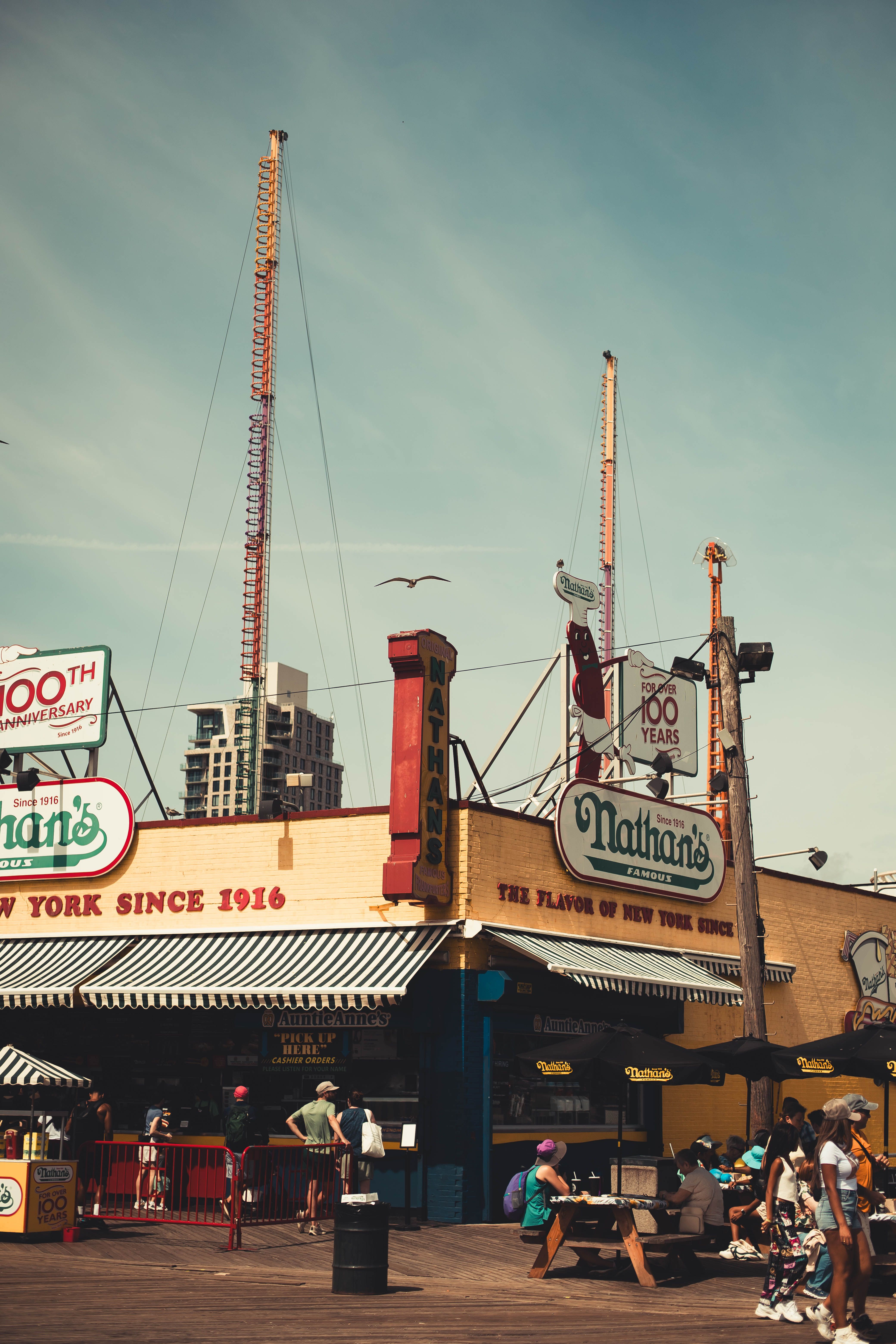 Iconic Nathan's Famous Hot Dogs stand at Coney Island with roller coaster in background.