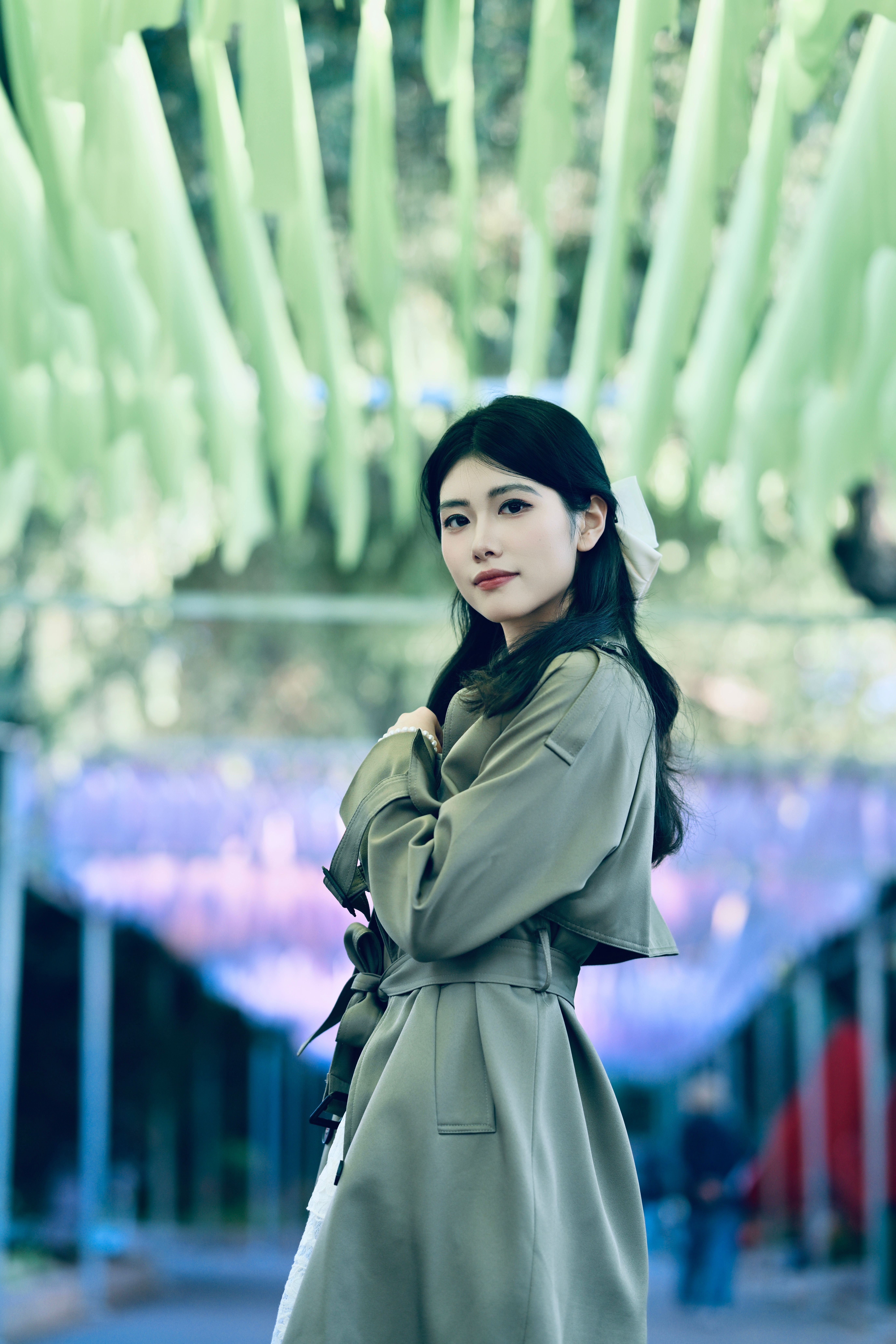 Young woman standing under vibrant, outdoor canopy wearing a stylish trench coat.