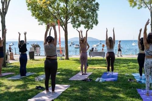 Free Group practicing yoga outdoors by the sea with a backdrop of sailboats and a clear blue sky. Stock Photo