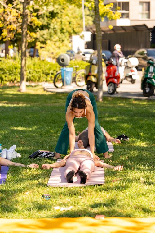 Free A group outdoor yoga session, featuring an instructor assisting a participant in a yoga pose in a park setting. Stock Photo