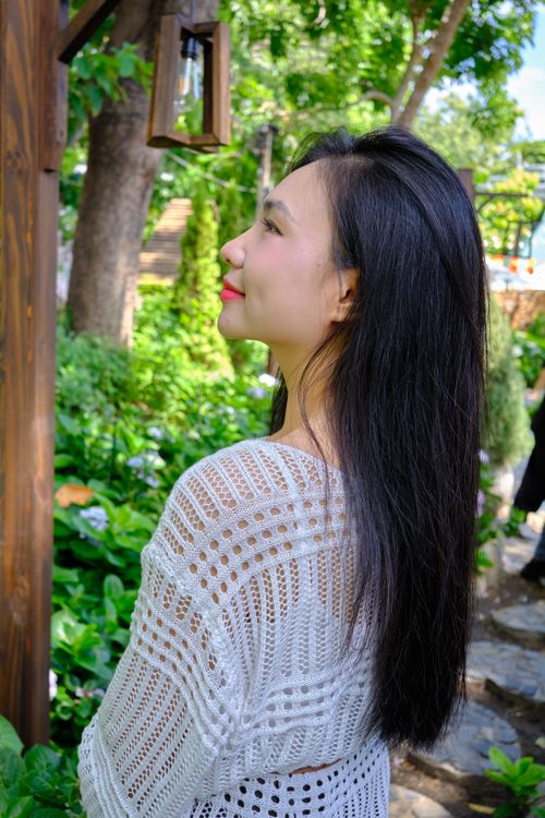 Free Profile of a woman in a white knit enjoying a sunny garden day. Stock Photo