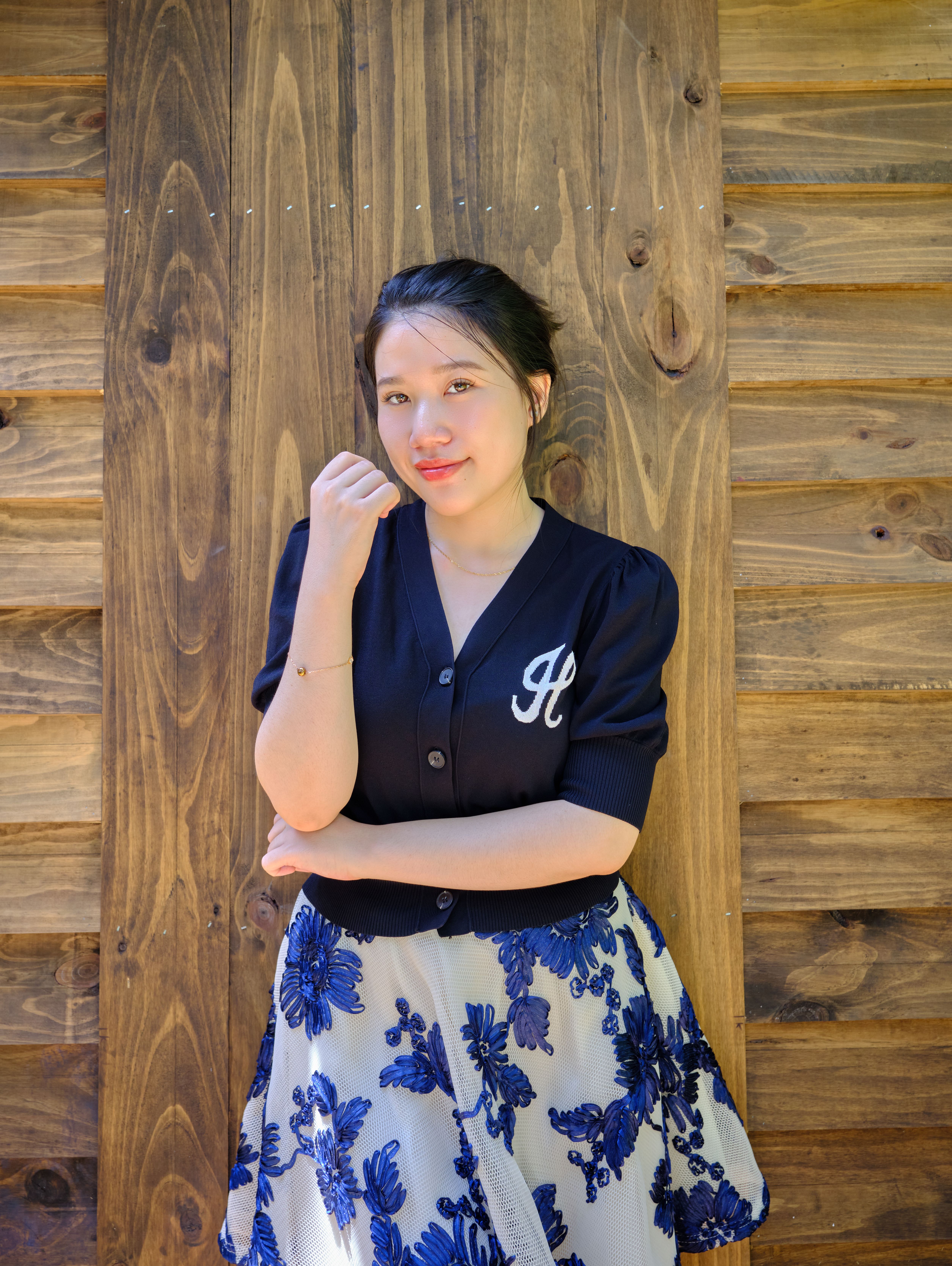 Young woman posing confidently in a floral skirt against a wooden backdrop.