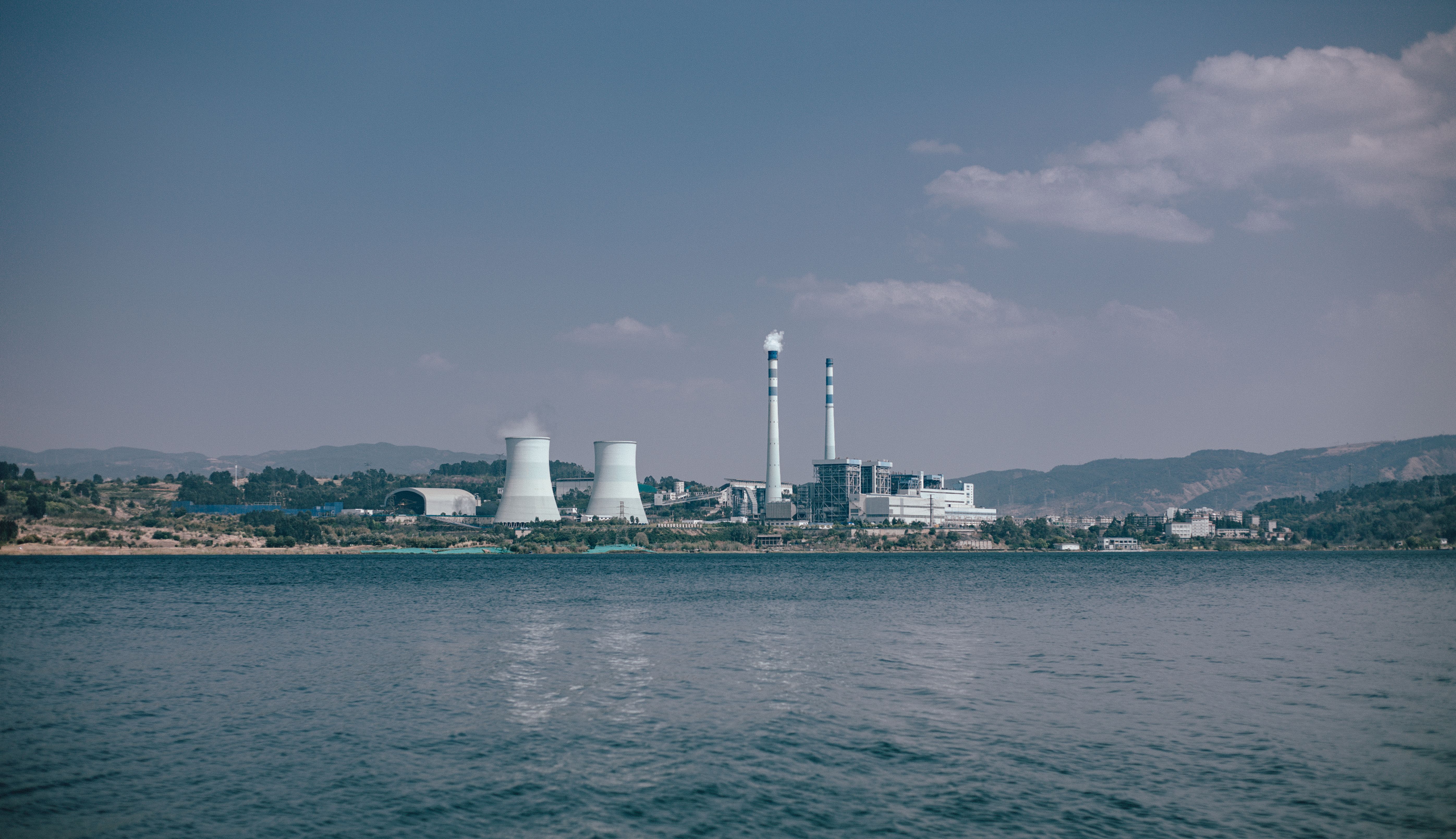 Cooling towers and chimneys of a power plant viewed from across a lake.