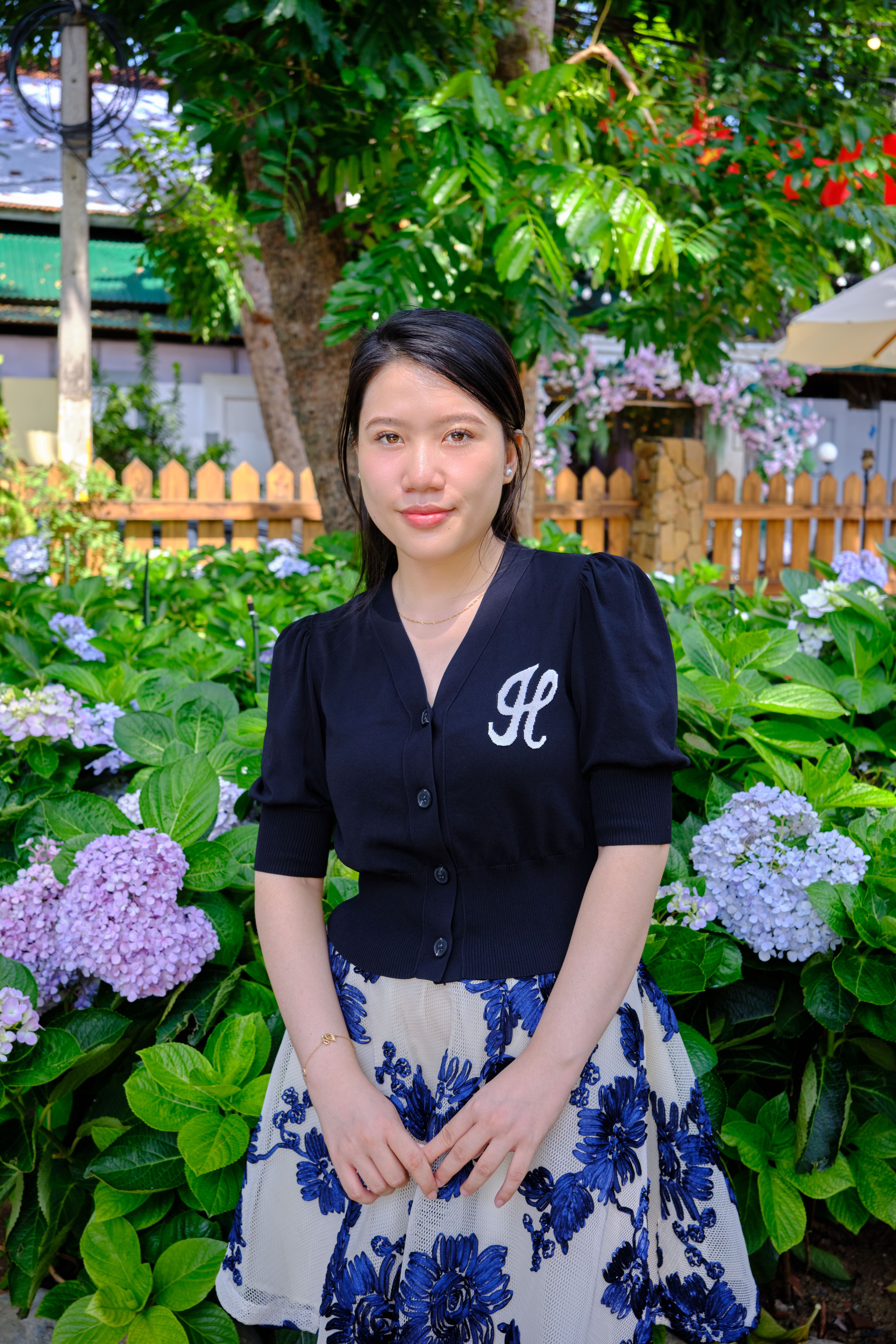 A woman stands confidently amidst blooming hydrangeas in a lush garden setting.