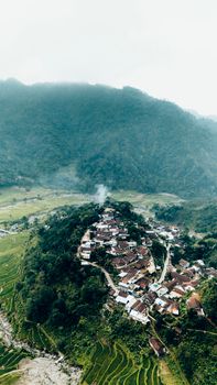 Serene aerial shot of an Indonesian village nestled in lush hills and rice terraces of Central Java. - Fotografer Sidoarjo