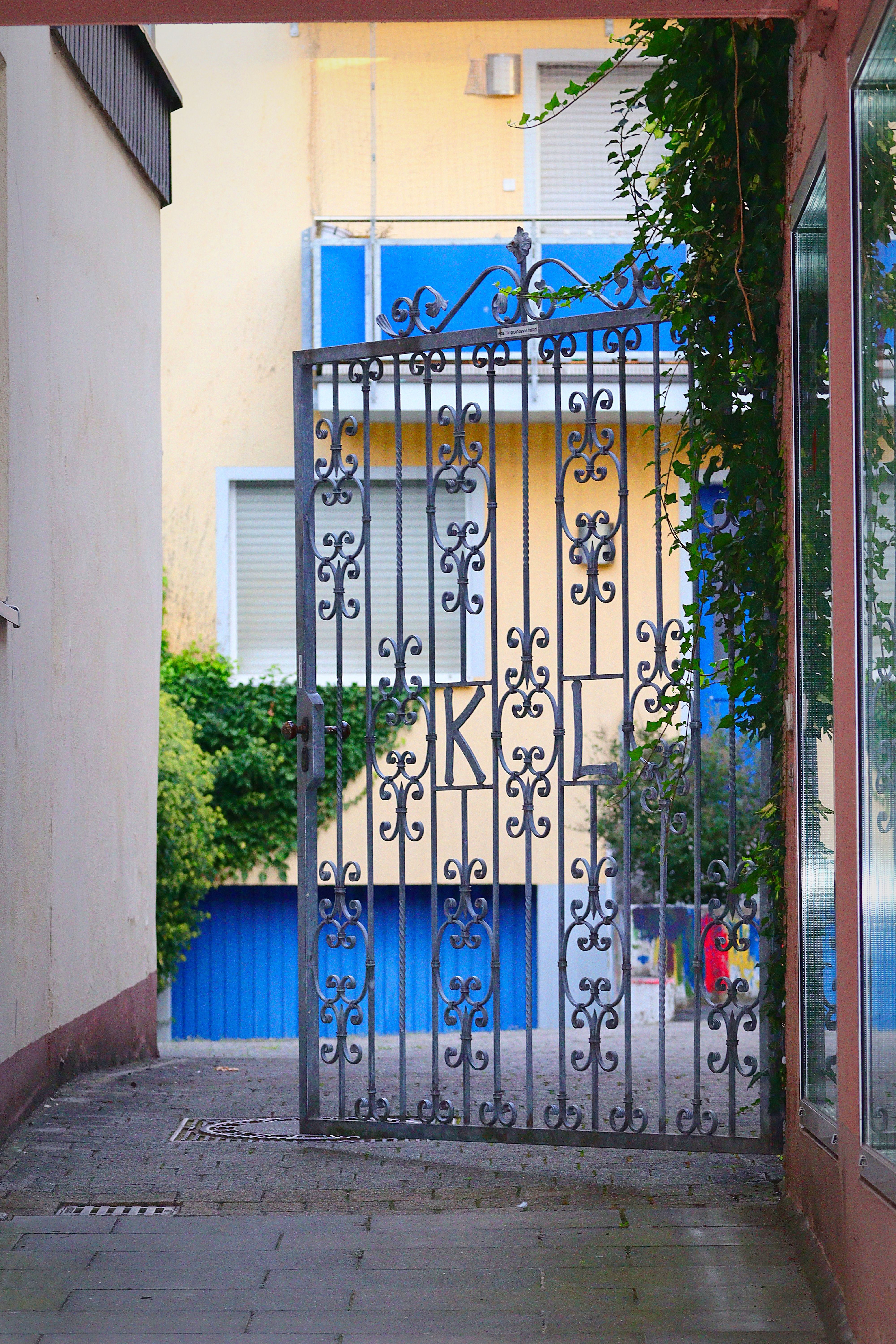 Decorative iron gate in a narrow alley with colorful urban backdrop.