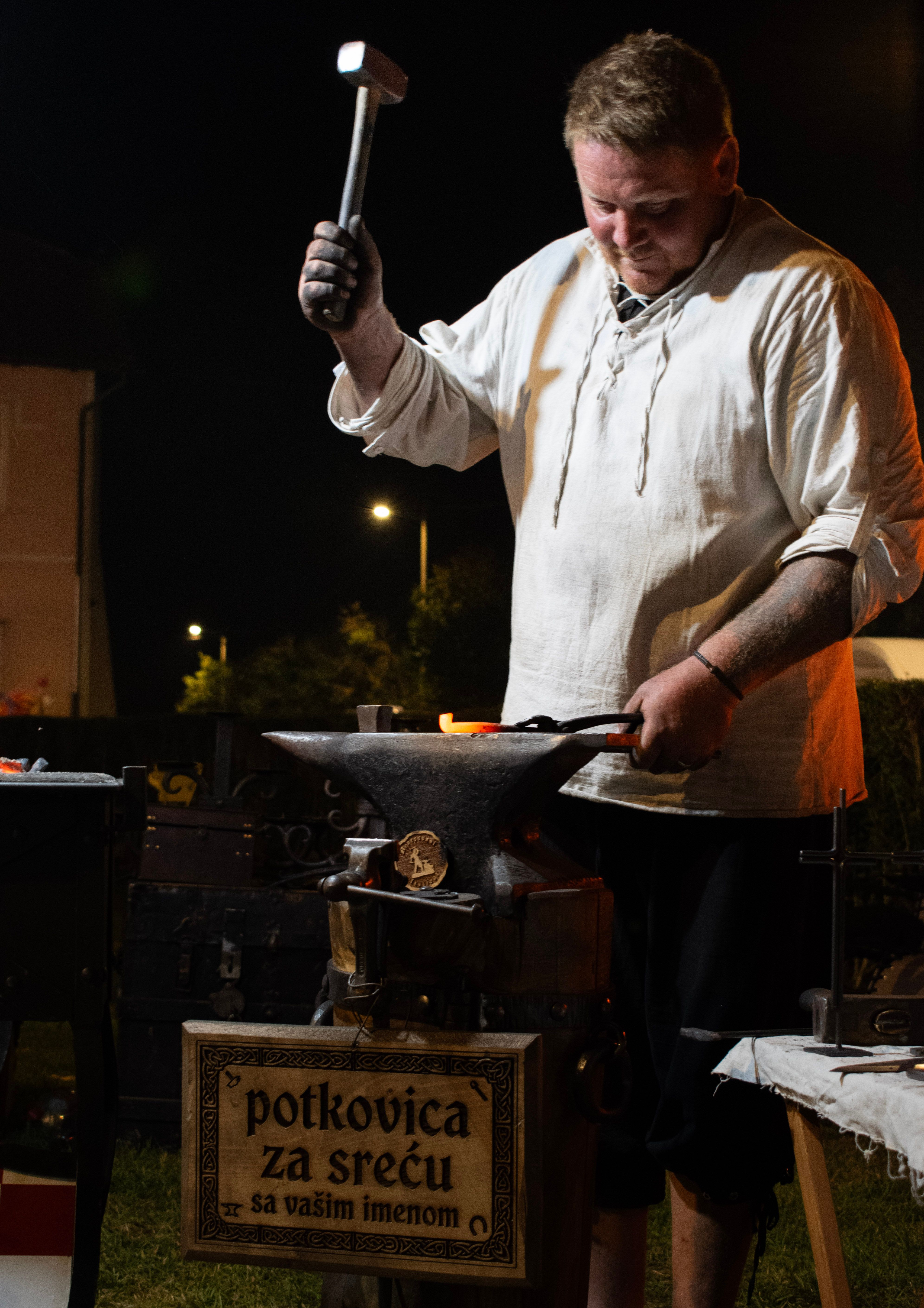 A traditional blacksmith crafting a lucky horseshoe outside at night in Voloder, Croatia.
