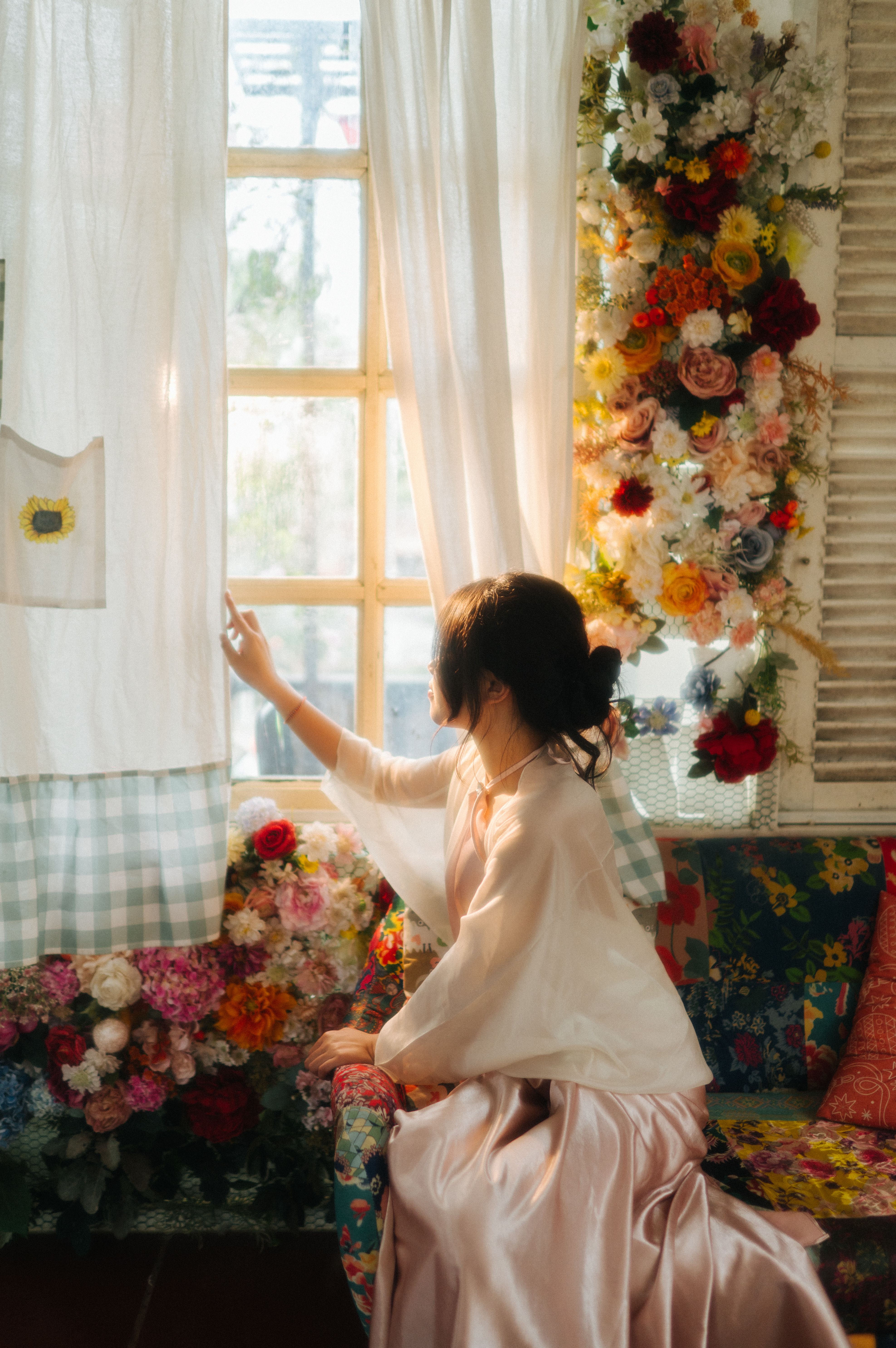 Serene scene of a woman in a floral-decorated room, gazing out a sunlit window.
