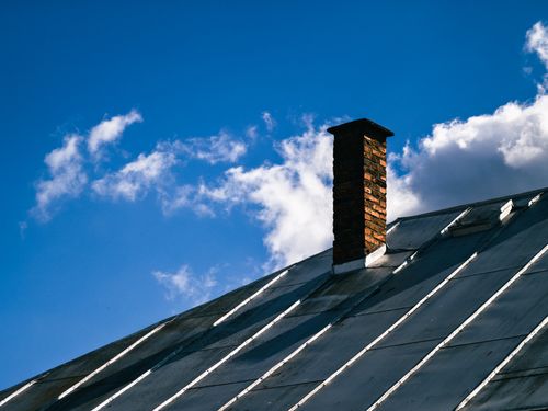 Free A scenic view of a metal roof with a brick chimney under a clear blue sky adorned with fluffy white clouds. Stock Photo