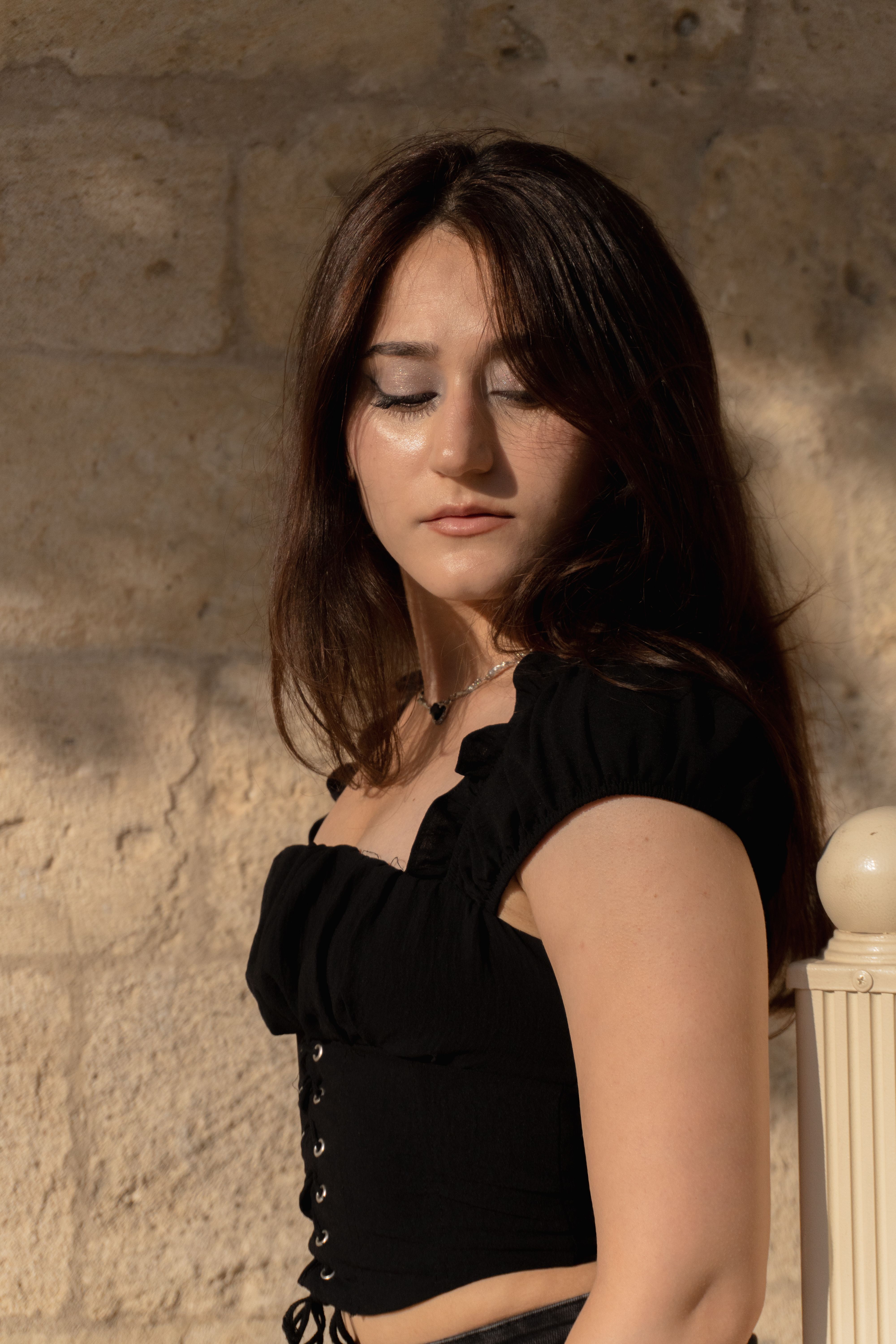 Portrait of a young woman in the sun, standing against a textured stone wall in Baku, Azerbaijan.