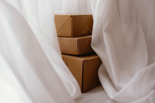 Free Cardboard boxes hidden behind a flowing white curtain, creating a soft indoor scene. Stock Photo