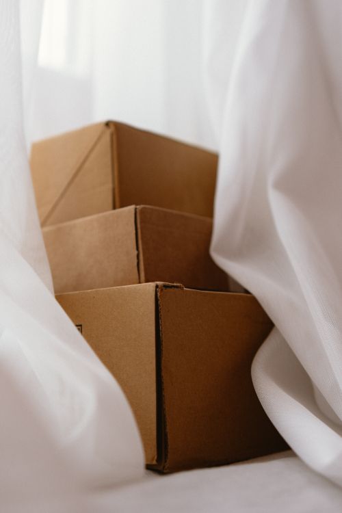 Free Three brown cardboard boxes partially obscured by white curtains, conveying a sense of mystery and storage. Stock Photo