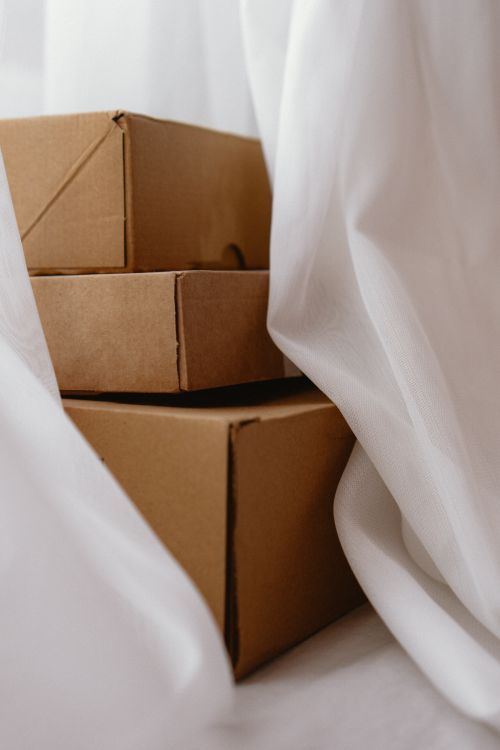 Free Three cardboard boxes partially concealed by flowing white curtains, creating a soft and serene atmosphere. Stock Photo