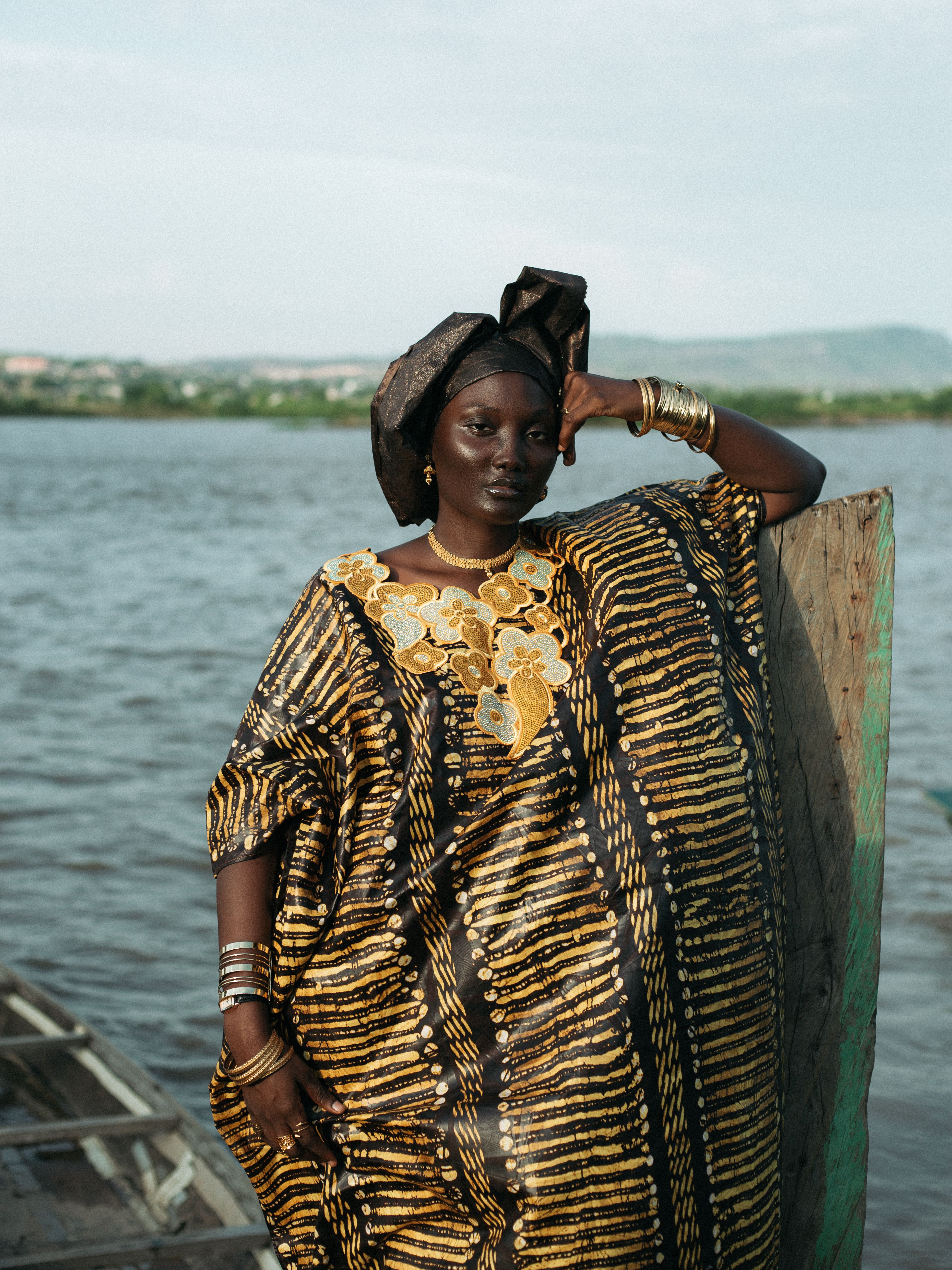 Elegant woman in traditional dress poses by a river, showcasing cultural richness.