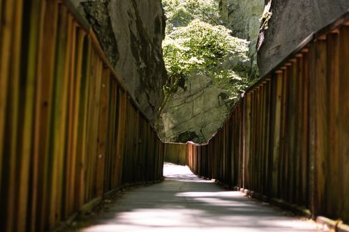 Free A peaceful wooden pathway meanders through a rocky gorge under bright sunlight. Stock Photo
