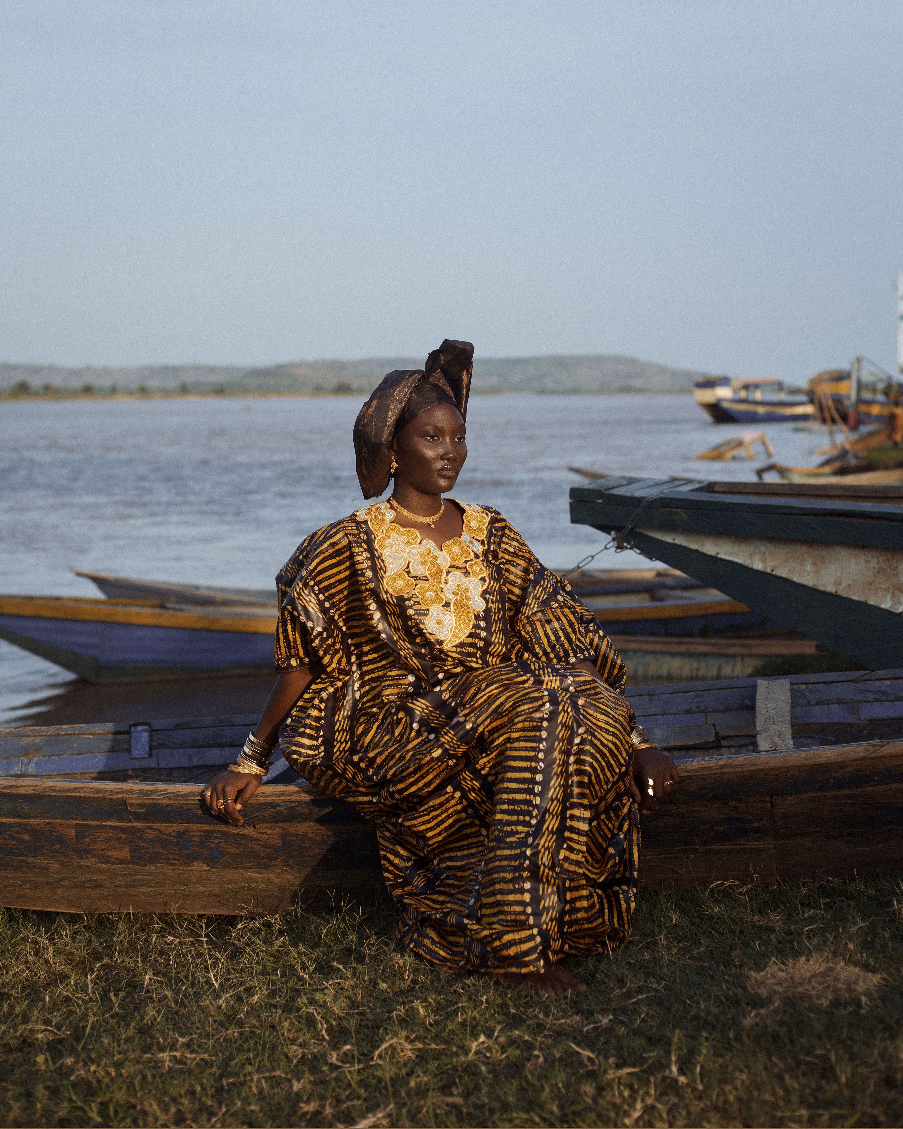 A woman in vibrant traditional attire sits by a riverside, conveying cultural elegance.