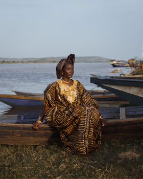 A woman in vibrant traditional attire sits by a riverside, conveying cultural elegance.