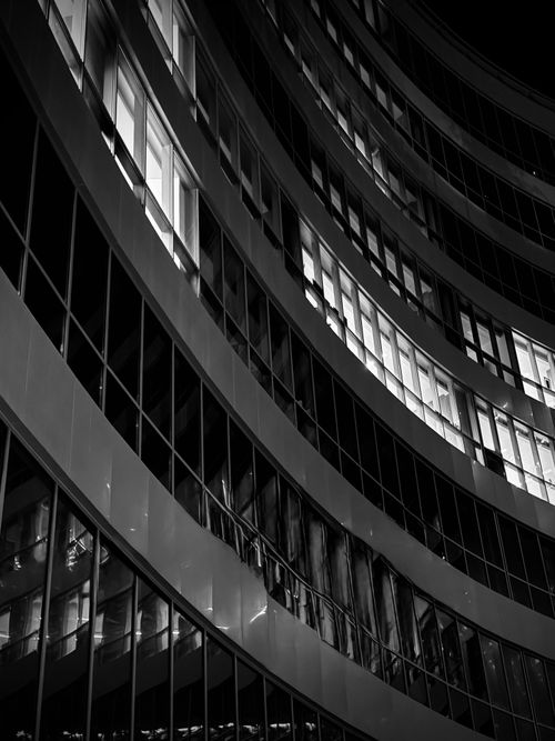 Free Abstract black and white photo of modern building architecture featuring sleek curved lines and windows at night. Stock Photo